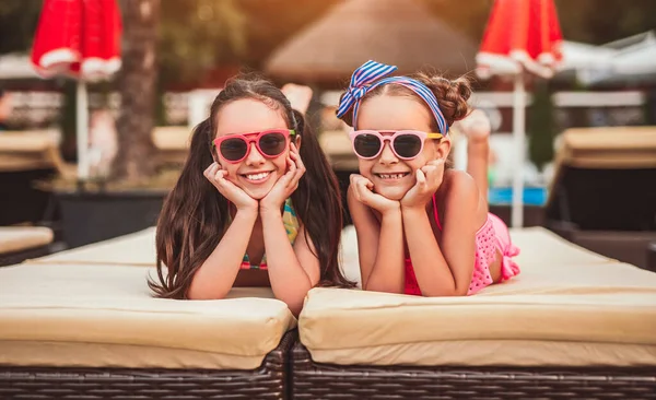 Meninas pequenas felizes que refrigeram junto à piscina — Fotografia de Stock