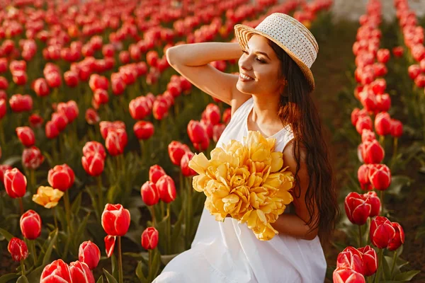 Радісна жінка з букетом, що сидить на полі тюльпанів — стокове фото