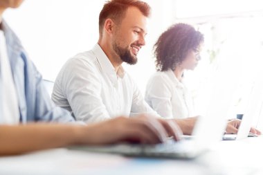 Genç meslektaşlar ofiste dizüstü bilgisayarlarla çalışıyorlar.