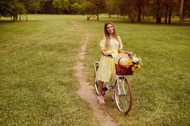Cheerful young female sitting on bike near path