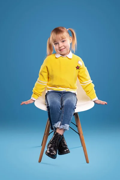 Aranyos kislány ül a széken és mosolyog a kamerába. — Stock Fotó