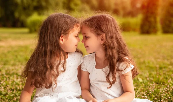 Glada Små Tvillingflickor Identiska Vita Klänningar Sitter Tillsammans Grönt Gräs — Stockfoto
