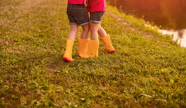 穿着类似衣服和橙色长统靴的无名小女孩在池塘边玩耍 他们在一起玩得很开心 — 图库照片