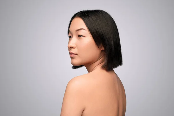 Молодая азиатка с обнаженной спиной смотрит в сторону — стоковое фото