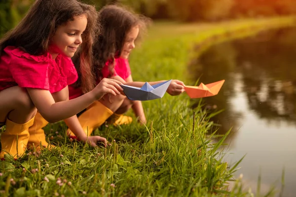 Irmãs brincando com barcos de papel perto do lago — Fotografia de Stock