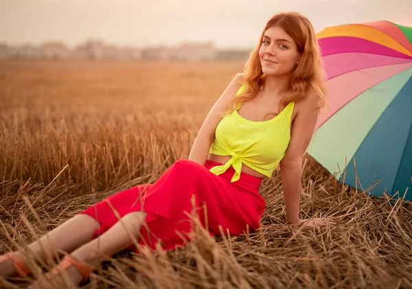 Mujer relajada sentada en hierba seca cerca del paraguas —  Fotos de Stock