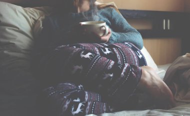 Kız beyaz bir yatakta bir fincan kahve ile.