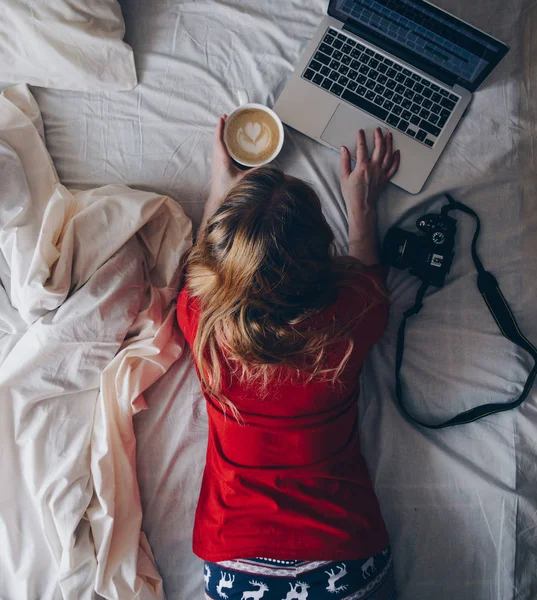 女孩在一张白色床与杯子咖啡和膝上型电脑 — 图库照片