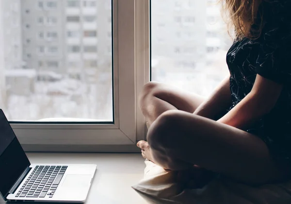 Girl in a dress on the window sill with a laptop.