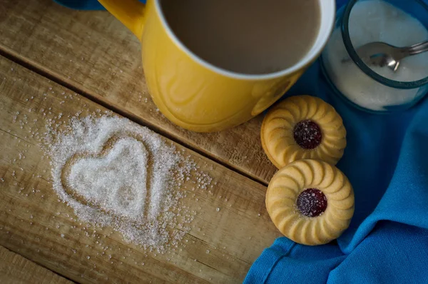 Vista superior da caneca com café leitoso, dois biscoitos doces, guardanapo azul e açúcar em forma de coração na mesa de madeira — Fotografia de Stock
