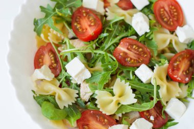 Farfalle, cherry domates, roket yaprakları, ıspanak, tavuk eti ve beyaz peynir beyaz kase ile makarna salatası. Sağlıklı salata. Dengeli yemek