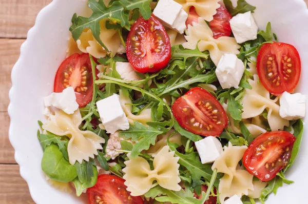 Farfalle makarna, beyaz peynir, dilimlenmiş domates, Bebek ıspanak yaprakları, roka, tavuk eti beyaz bir kase salata. Yukarıdan görüntüleyin. Sağlıklı makarna salatası