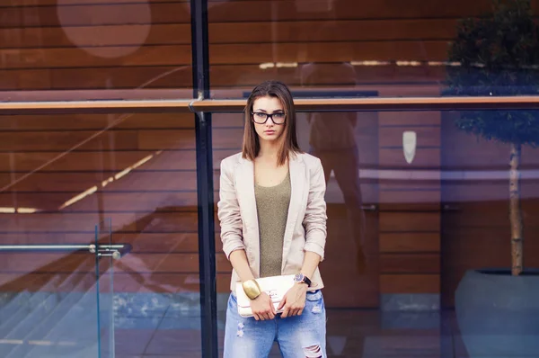 Youn modelo feminino europeu com óculos, bob corte penteado, jaqueta casual bege, jeans azuis e embreagem dourada — Fotografia de Stock