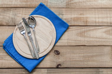 Arka plan ile yuvarlak ahşap tahta ve mavi peçete gümüş yemek takımı. Bıçak, çatal ve kaşık ahşap tablo