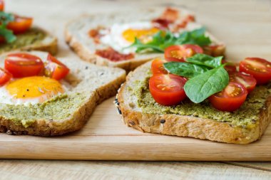 Kahvaltı tost multicereal ekmek, pesto sos, domates, yumurta, ıspanak ahşap kesme tahtası üzerinde. Sağlıklı kahvaltı. Dengeli yemek 