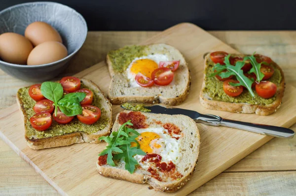 Tost ile tahıl ekmeği, yumurta, roka, domates, ıspanak yaprakları, ahşap kesme tahtası üzerinde hizmet pesto ve domates sosu. Kahvaltı yemek. Sağlıklı beslenme