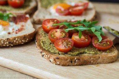 Sebze ile kahvaltı tost. Sandviç çok tahıl ekmek, pesto sos, kırmızı kiraz domates, roka ahşap tahta üzerinde. Sağlıklı beslenme