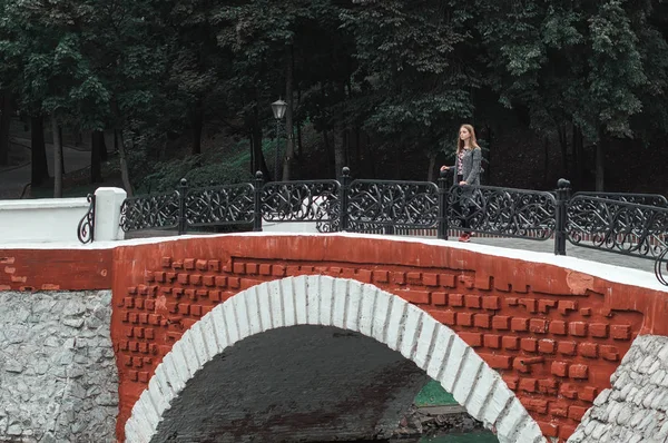 Una adolescente con abrigo de punto parada en el puente del parque. Humor otoñal. Rojo y verde — Foto de Stock