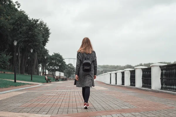 Adolescente femenina con mochila negra, pantalones vaqueros negros y cárdigan de punto gris caminando por el parque — Foto de Stock