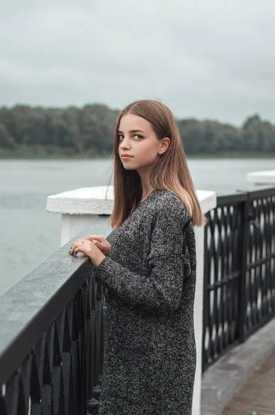 Potret vertikal remaja perempuan dengan rambut pirang dan mata biru berdiri di jembatan dekat sungai — Stok Foto
