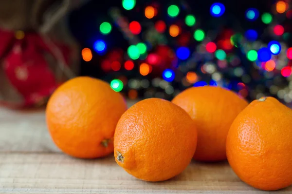 Несколько апельсинов на деревянном столе, размытые огни в качестве фона. Новогодняя и рождественская атмосфера — стоковое фото