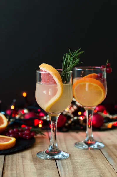 Winter vitamin cocktail with grapefruit, rosemary, orange and red currant in wine glasses served on wooden table with christmas lights — Stock Photo, Image