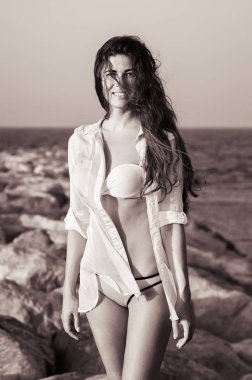 Mutlu gülümseyen kadın giyen bikini ve beyaz gömlek ayakta büyük taşlar, portresi. Kumsalda genç kadın fotoğrafı siyah-beyaz