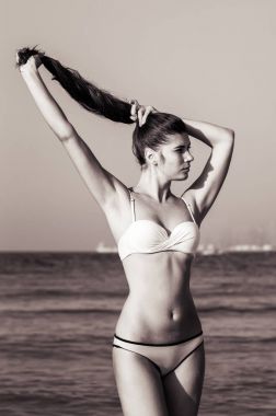 Siyah ve beyaz kadın portre. Genç kadın uzun saçlı plajda bikini ayakta su yakınında giyiyor