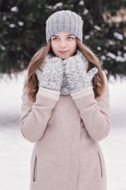 Dikey sıcak giysiler içinde genç bir kadın portresi: bej bir palto, eşarp, eldiven ve şapka örme. Kış hava. Giyim Kış