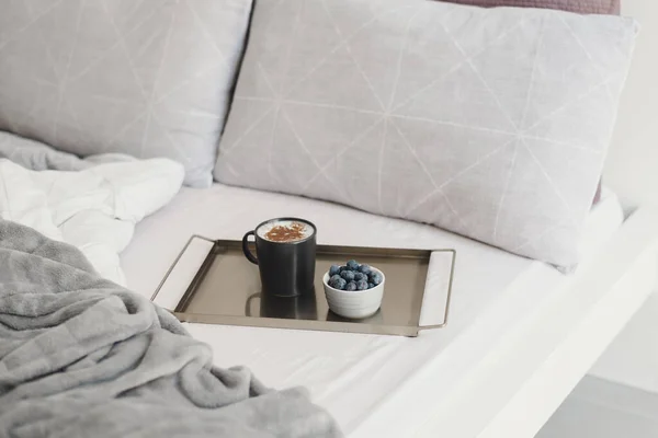 Coffee with cinnamon powder and fresh blueberry on metal tray served in bed. Cozy morning. Breakfast in bed concept