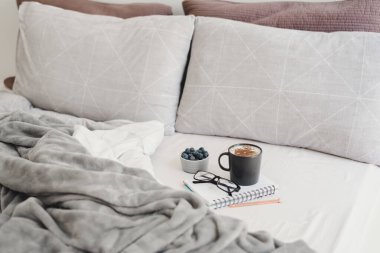 Yatakta hafif bir kahvaltı. Yatak odasından çalışmak: tarçınlı kapuçino kahvesi, yabanmersini, not defteri, kalem ve bardak. Yatak konseptinden çalış