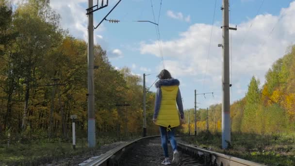 Девушка идет по рельсам осенью — стоковое видео