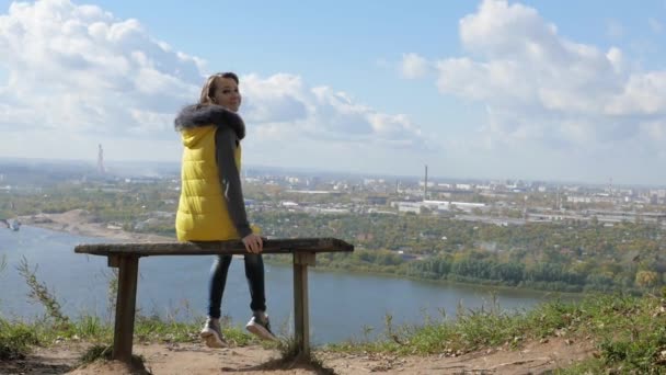 Девушка сидит на скамейке и смотрит на панораму города — стоковое видео