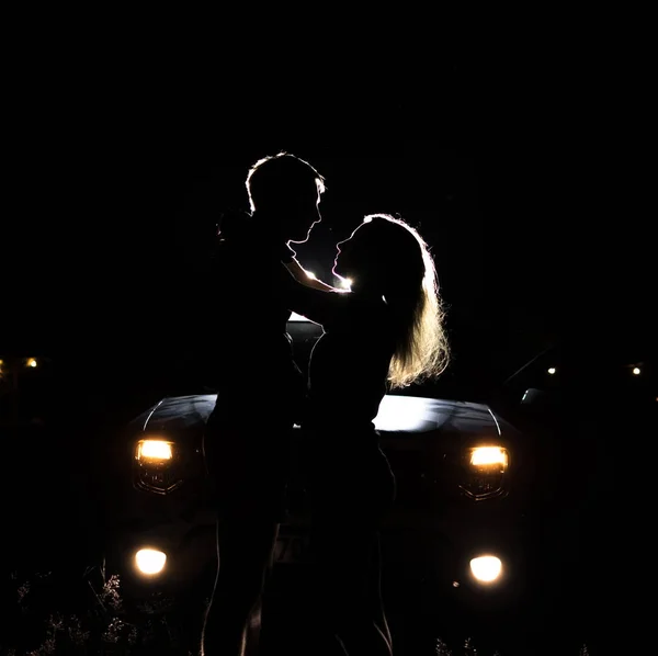 Siluetas de personas en la noche en la luz de los faros de un coche — Foto de Stock