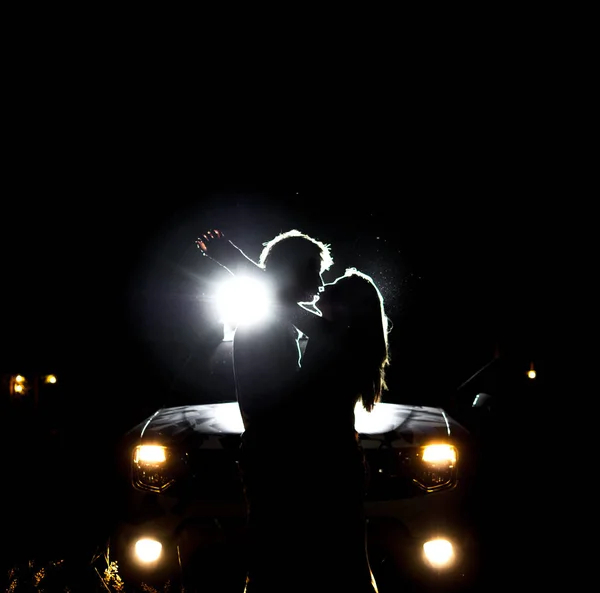 Silhouette di persone di notte alla luce dei fari di una macchina Foto Stock Royalty Free