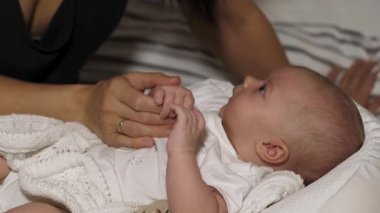 Sevimli bebek annesinin parmaklarını tutuyor ve beşikte yatıyor.