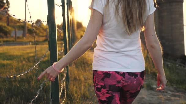 Het Meisje Loopt Langs Het Hek Bij Zonsondergang Raakt Zijn — Stockvideo