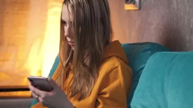 Bir kız kanepede otururken ödemeyi telefonundan laptopuna aktarıyor.