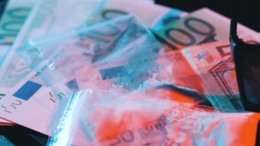 Para, dizüstü bilgisayar, gözlük ve eroin neon ışıkta masanın üstünde.