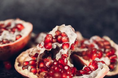 Açık bir nar (meyve), yeşil bir dalı olan gri bir arka planda, masanın üzerinde yatar.