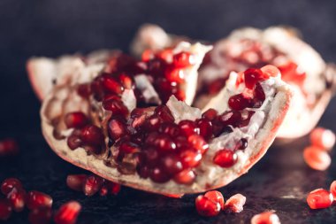 Açık bir nar (meyve), yeşil bir dalı olan gri bir arka planda, masanın üzerinde yatar.