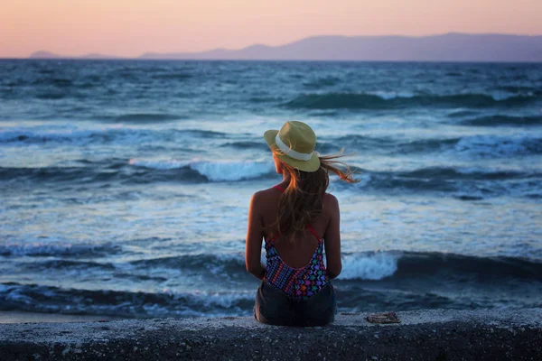 Joven chica hermosa sentada cerca del mar al atardecer en verano —  Fotos de Stock