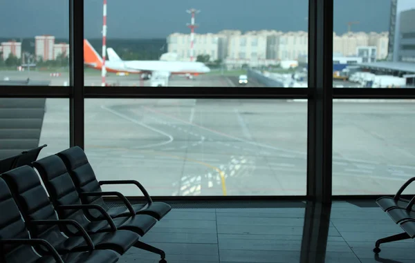 Sitze in Großaufnahme auf dem Flughafen im Wartezimmer für die Abreise. Im Hintergrund ein Fenster und eine Landebahn mit Flugzeugen — Stockfoto