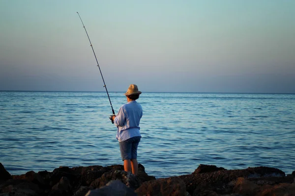 Žena v klobouku je rybolov s rybářským prutem v ruce na mořském pobřeží — Stock fotografie