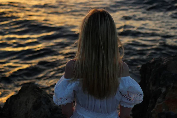 Joven hermosa chica rubia sentada de cerca cerca del mar al atardecer —  Fotos de Stock