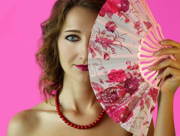 Parlak makyaj ve eller yakın çekim pembe arka plan üzerinde bir fan ile güzel bir genç kız portresi