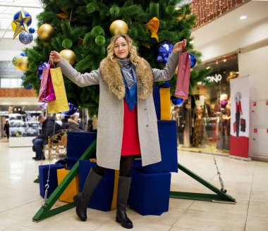 Genç güzel kız bir Noel ağacı arka plan üzerinde parlak paketleri ile bir alışveriş merkezindeki alışveriş hoşlanır