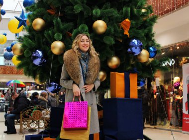 Genç güzel kız bir Noel ağacı arka plan üzerinde parlak paketleri ile bir alışveriş merkezindeki alışveriş hoşlanır