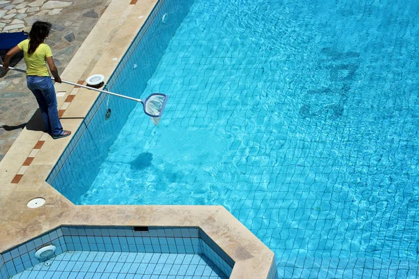 Uma mulher limpa a piscina de detritos e insetos durante o dia no verão — Fotografia de Stock