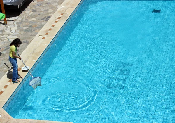 Een vrouw reinigt het zwembad uit puin en insecten tijdens de dag in de zomer — Stockfoto